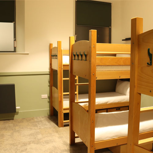 A bedroom with bunk beds. The walls are decorated in cream and green, and there are dark green blinds on the windows.